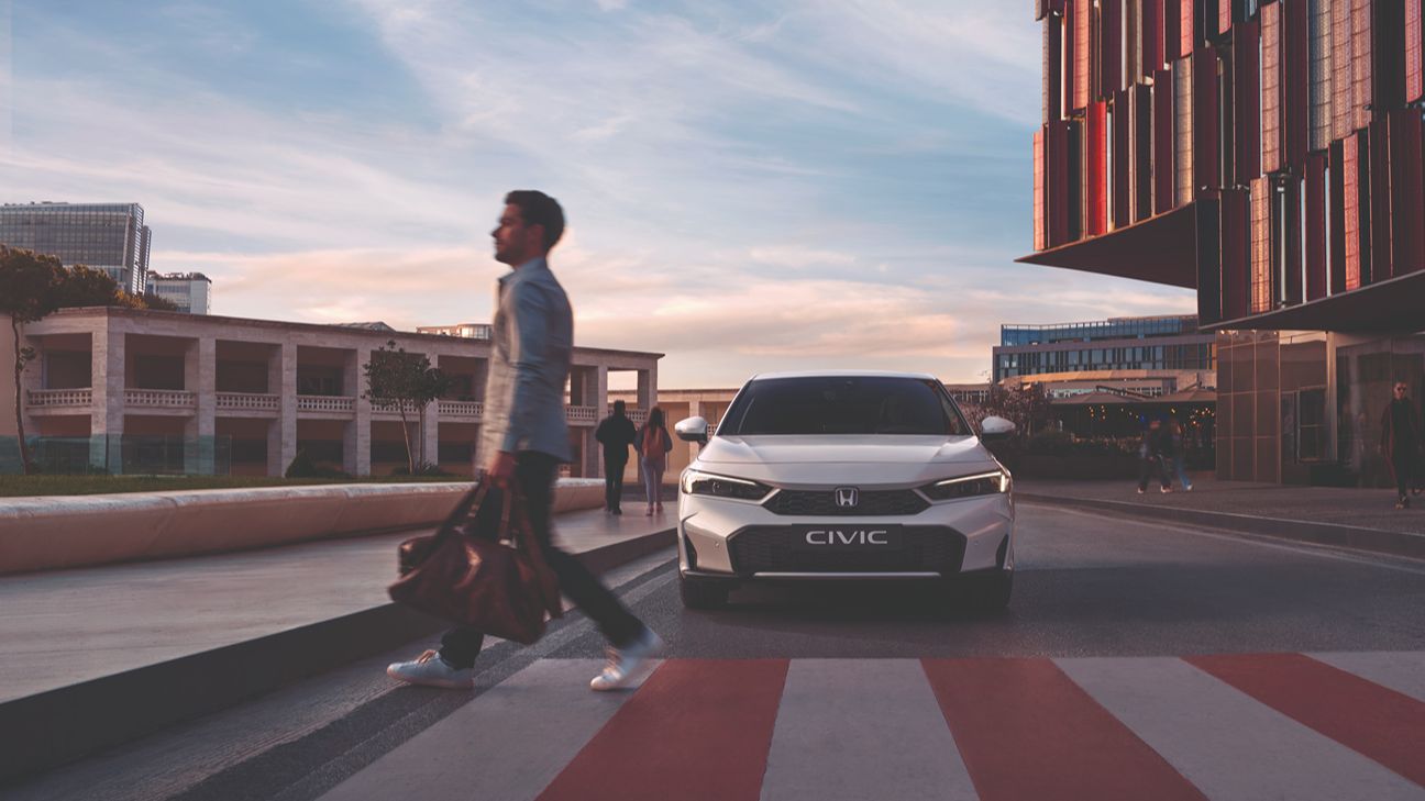 un uomo che attraversa la strada con una Honda Civic bianca sullo sfondo