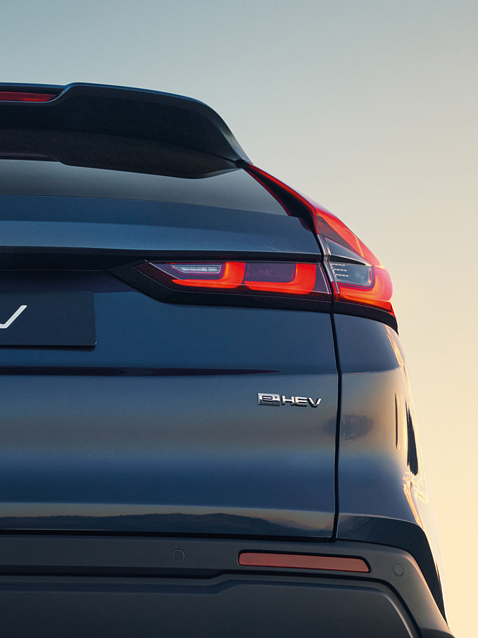 Dettaglio posteriore di una Honda CR-V e:HEV blu scuro che mostra il logo Honda, la scritta CR-V e le luci di posizione posteriori a LED di firma illuminate, contro un cielo al tramonto dai colori soffusi.