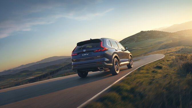 Vista posteriore laterale del SUV CR-V Hybrid blu in un ambiente montano.