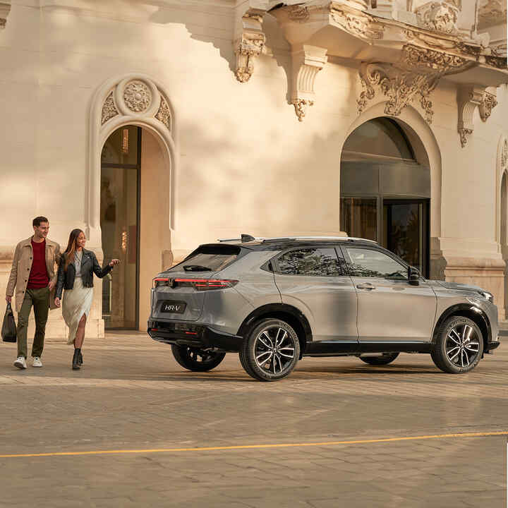 Coppia che cammina accanto a un HR-V parcheggiato fuori da un edificio. 