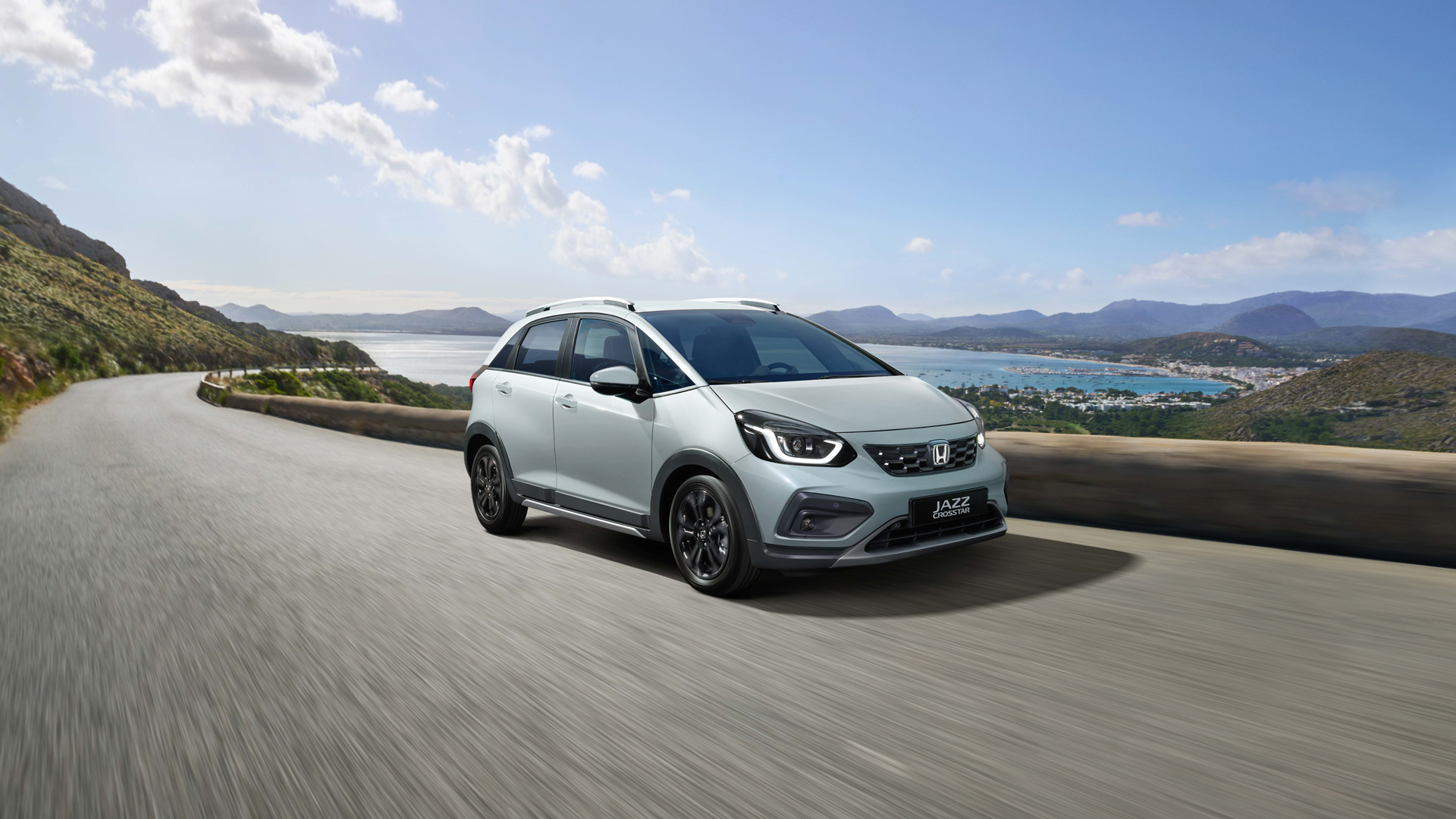 Vista anteriore di tre quarti di Honda Jazz Hybrid durante la guida, con una vista panoramica sullo sfondo.