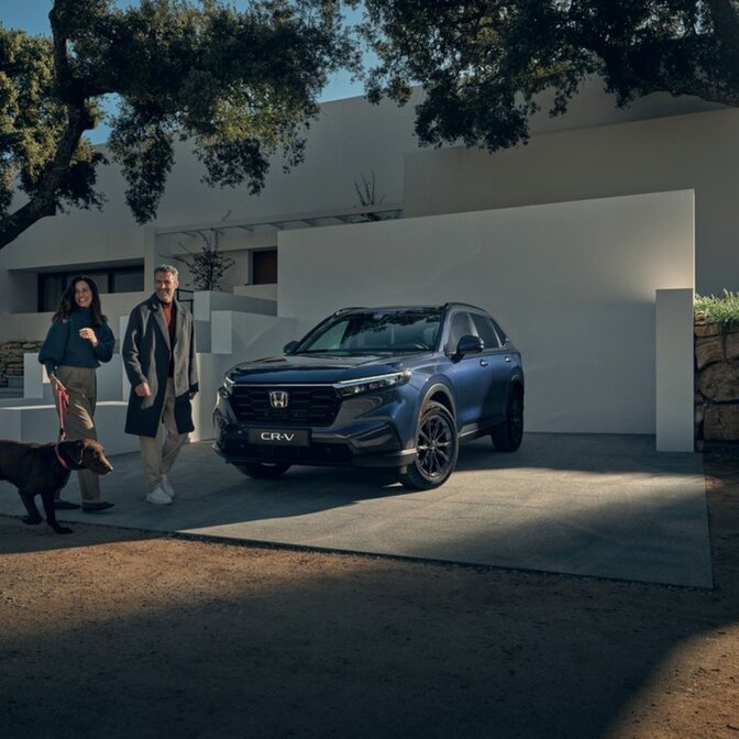 Una coppia porta a spasso un cane accanto a una Honda CR-V parcheggiata.