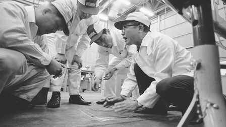 Soichiro Honda e un gruppo di operai che indossano una tuta da lavoro bianca.