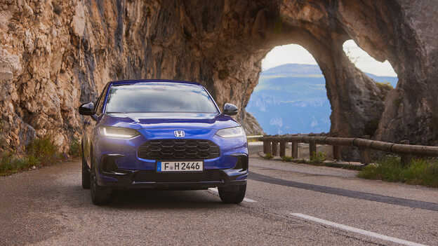SUV ZR-V Hybrid blu con propulsore sportivo guidato su una strada di montagna.