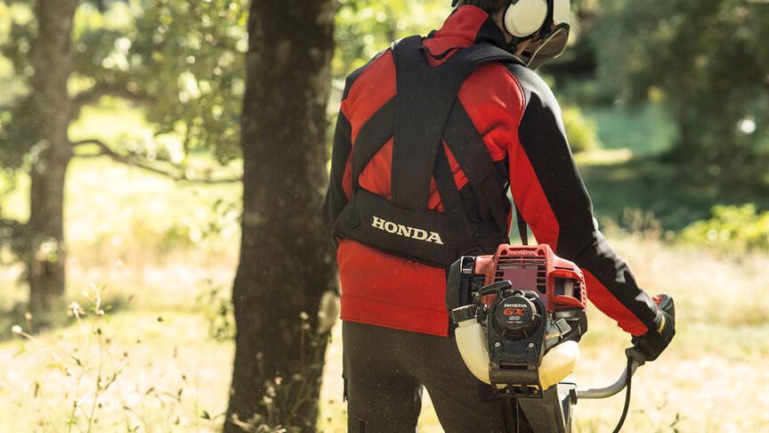 Modello con decespugliatore spalleggiato in un ambiente boschivo.