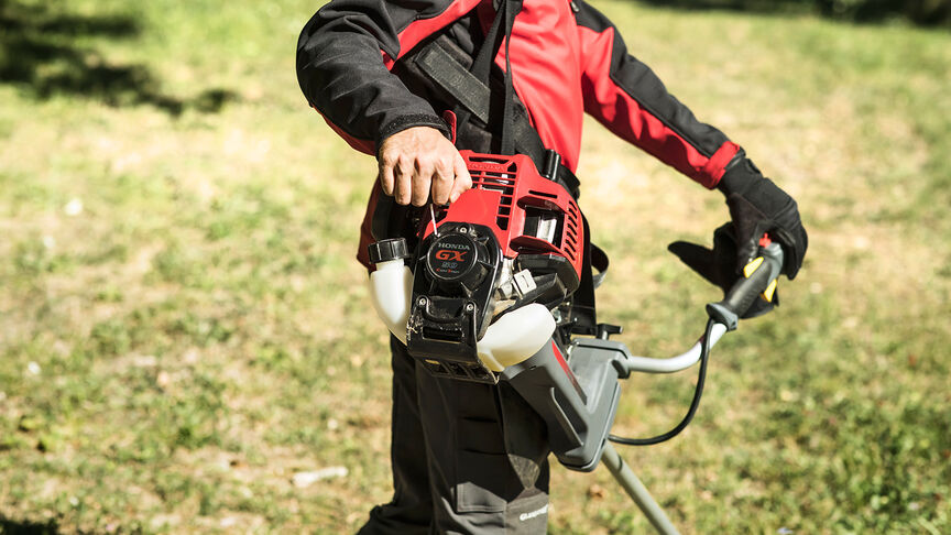 Modello con decespugliatore spalleggiato in un ambiente boschivo.