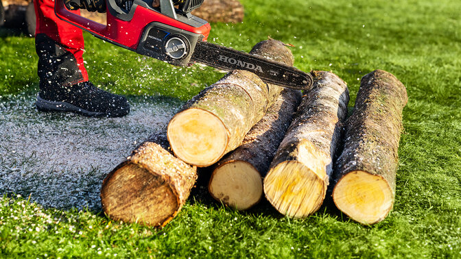 Primo piano di un uomo che usa la motosega a batteria Honda per tagliare il legno.