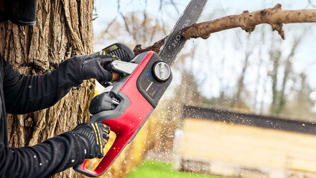 Primo piano del modello che taglia un ramo di un albero con una motosega a batteria.