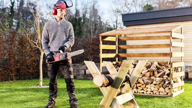 Uomo in giardino che utilizza una motosega a batteria.