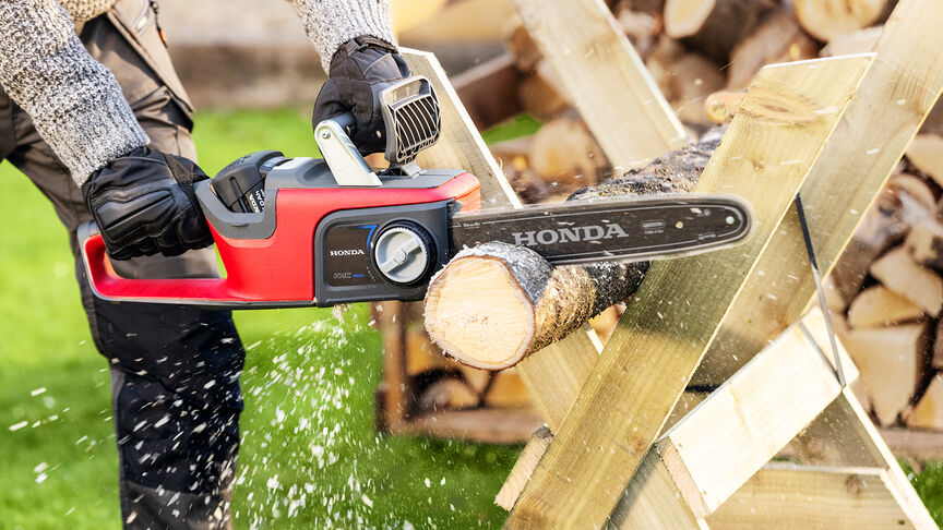 Primo piano di un modello che taglia il legno con una motosega a batteria Honda.