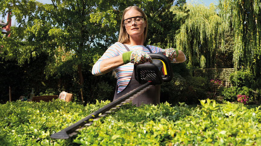 Donna che utilizza il tagliasiepi a batteria Honda per tagliare una siepe in un giardino.