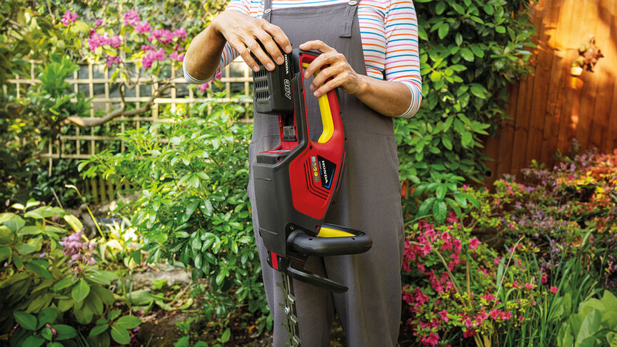 Donna che utilizza il tagliasiepi a batteria Honda per tagliare una siepe in un giardino.