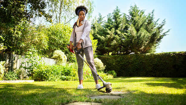 Donna che utilizza il decespugliatore a batteria Honda sull'erba in un giardino.