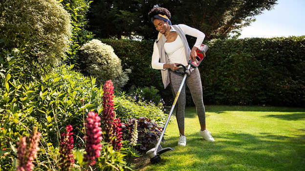 Femme utilisant une débroussailleuse à batterie Honda sur l'herbe dans un jardin et démontrant la protection des plantes.