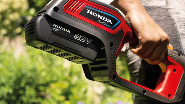 Gros plan d'un modèle tenant une débroussailleuse à batterie Honda