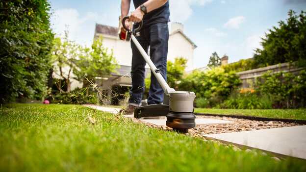 Uomo che utilizza il decespugliatore a batteria Honda sull'erba in un giardino.