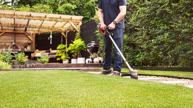 Uomo con il tagliasiepi a batteria Honda che taglia l'erba in un giardino.