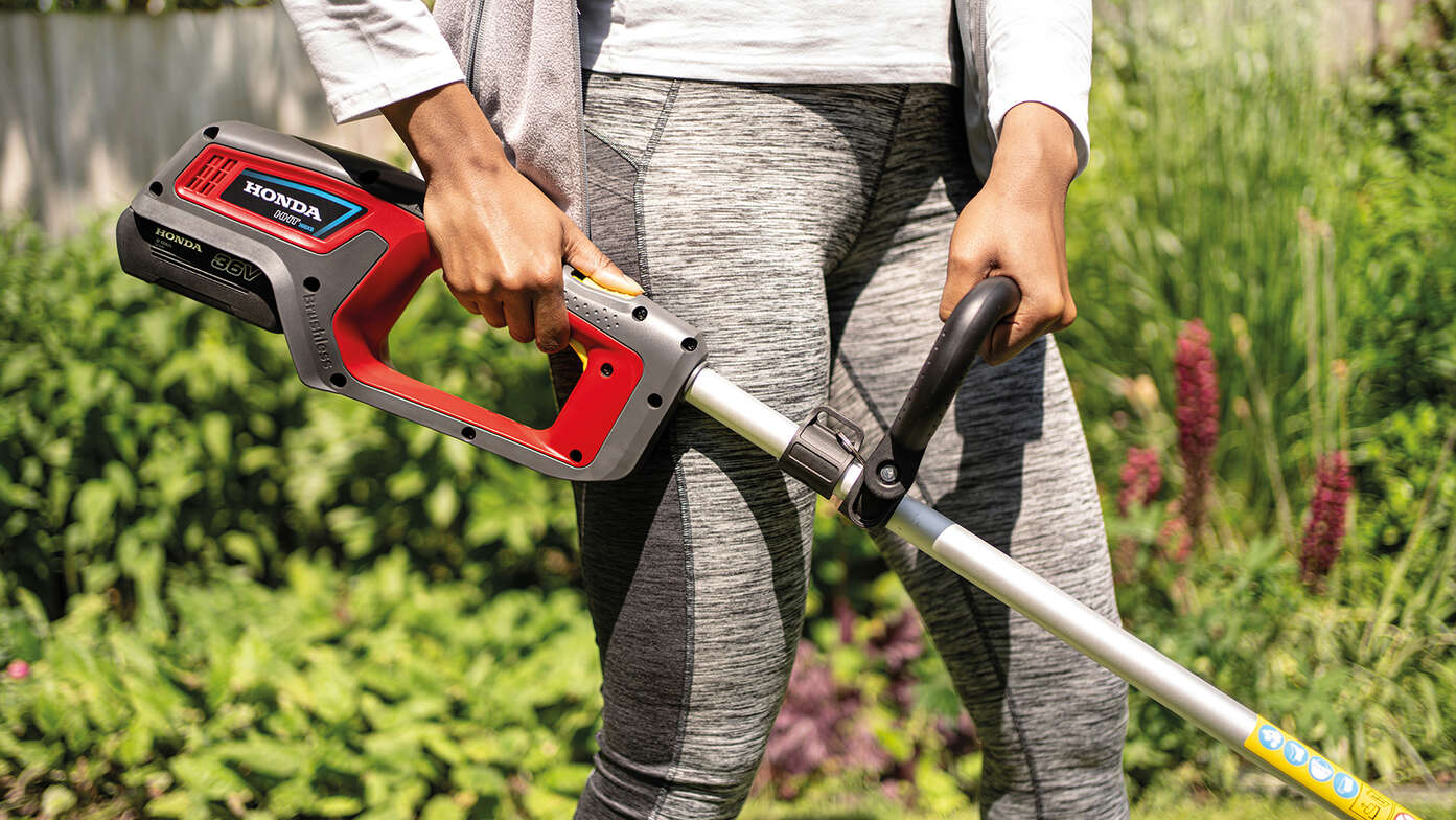 Primo piano di una donna che utilizza il decespugliatore a batteria Honda in un giardino.