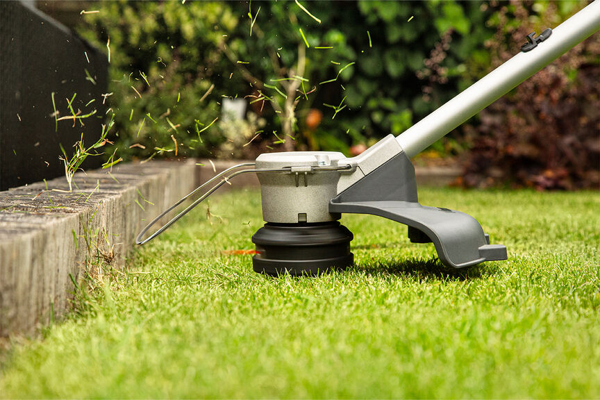 Débroussailleuse alimentée par batterie démontrant une ligne de coupe de haute qualité sur une pelouse.