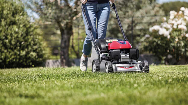 Vista laterale del rasaerba Honda IZY con una donna in giardino