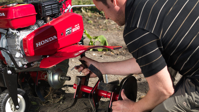 Operatore che collega un nuovo accessorio ad una motozappa, luogo di utilizzo: giardino.