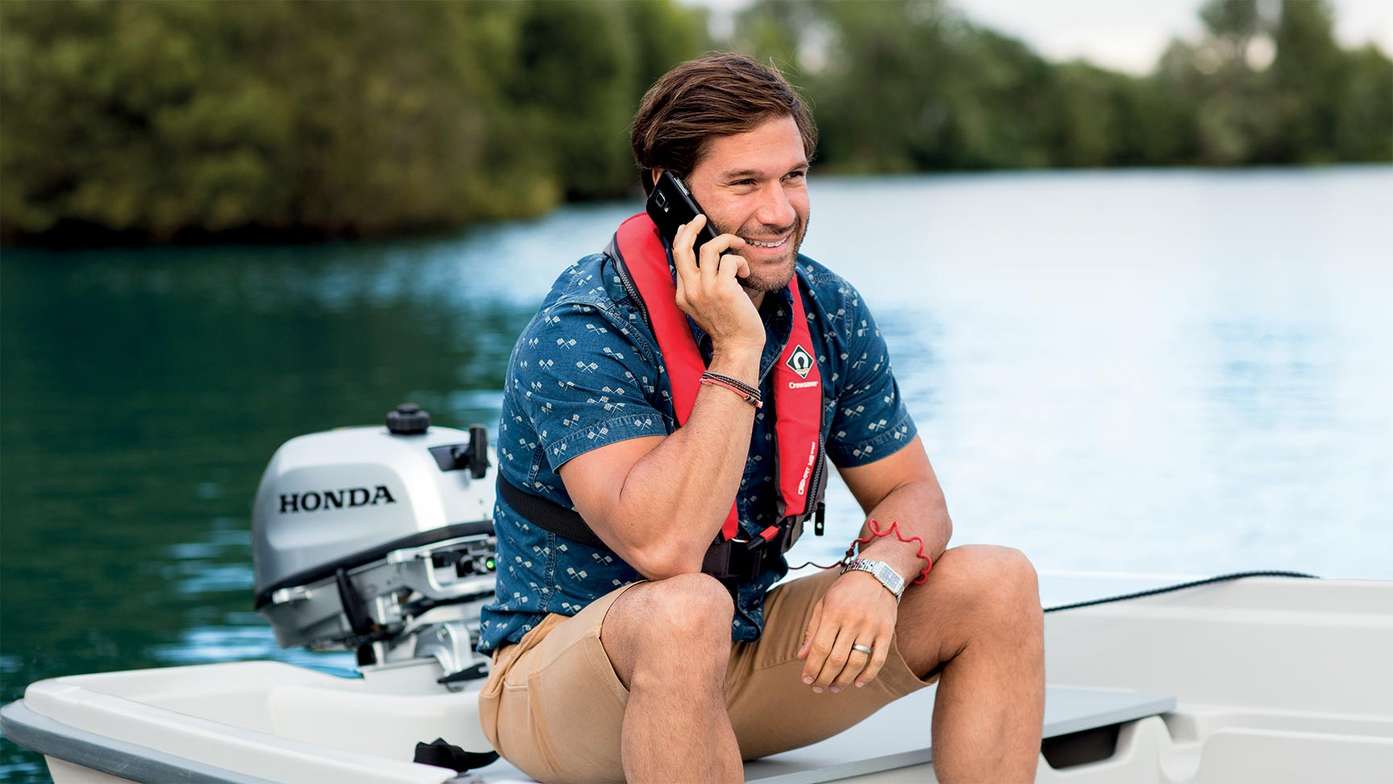 Uomo su una piccola barca che ricarica il telefono dal suo motore fuoribordo Honda mentre sta parlando