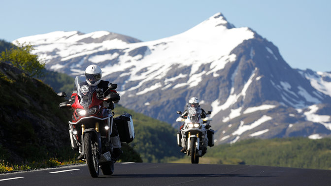 Due moto che percorrono la strada con le montagne innevate in lontananza.