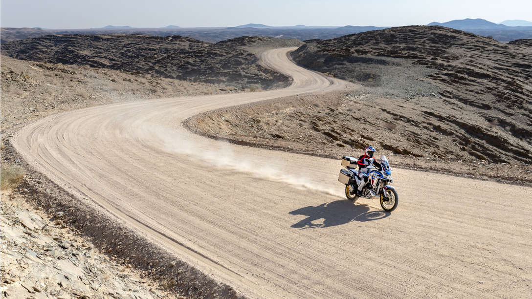 Honda Africa Twin Adventure Sports, inquadratura anteriore destra di tre quarti, guidata su una strada sterrata in un paesaggio desertico