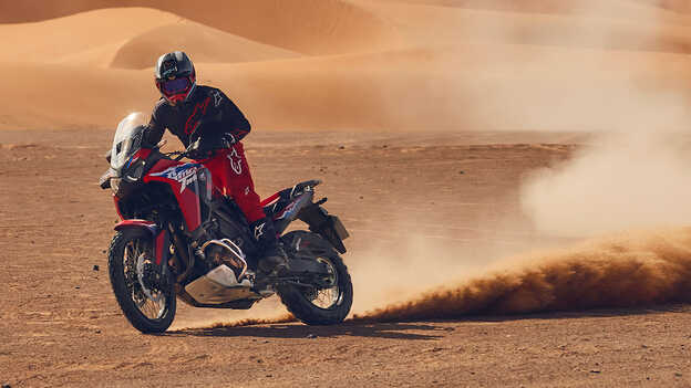 Modello alla guida di una moto CRF1100L Africa Twin in un luogo desertico.