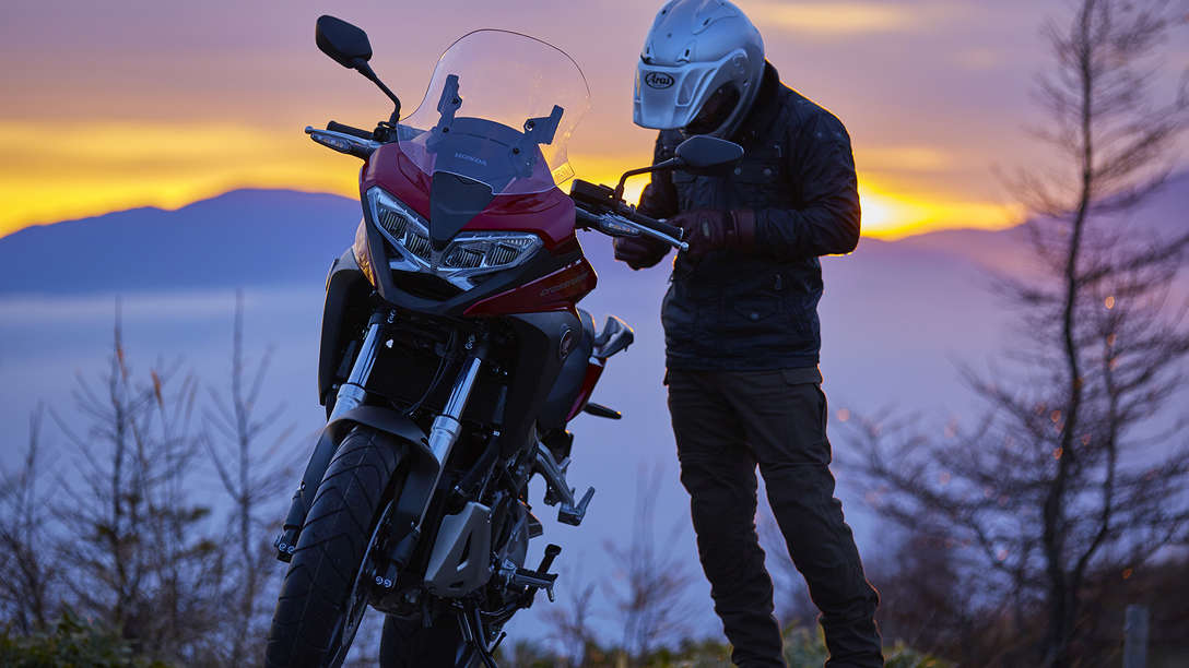 VFR800X parcheggiata in un ambiente rurale accanto al pilota in piedi.