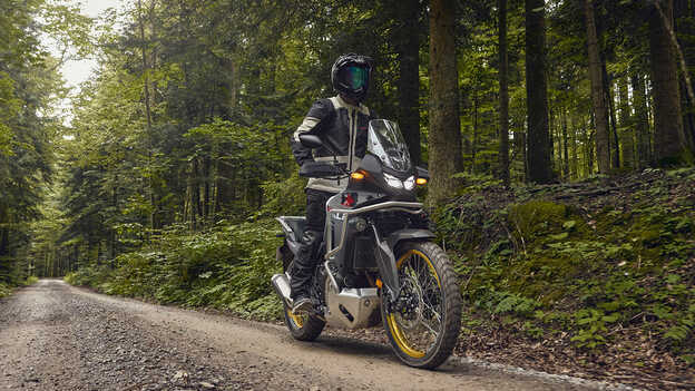 Pilota alla guida di una Honda XL750 Transalp in un luogo boschivo.