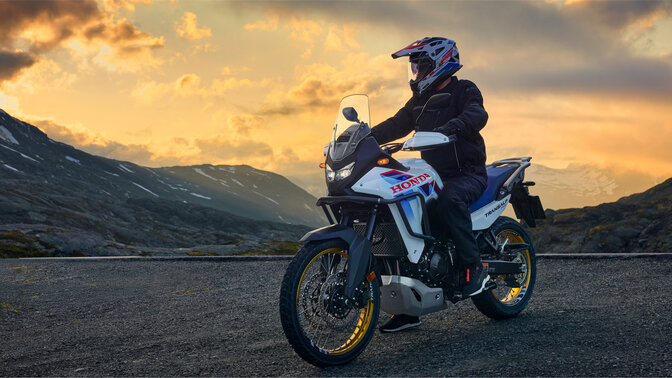 Modella alla guida di una motocicletta XL750 Transalp su strada in una località di montagna.