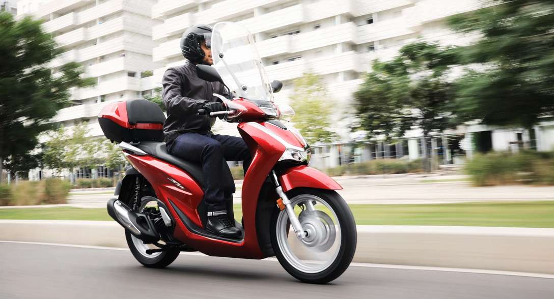 Honda SH125i, vista anteriore destra di tre quarti, con conducente, in città
