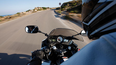 Inquadratura della strumentazione, del manubrio e della strada davanti alla moto da sopra le spalle del pilota.