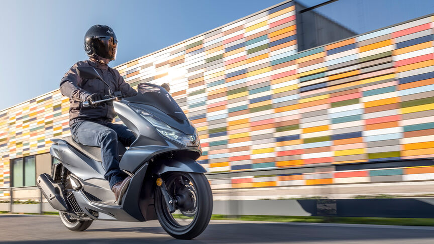 Honda PCX125 – Immagine dinamica posteriore di tre quarti con guidatore