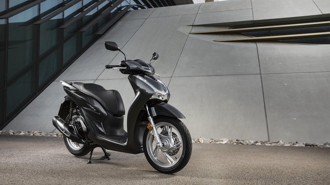 Honda Sh125i con bauletto e parabrezza su strada.