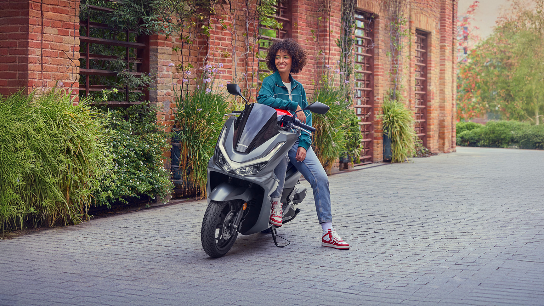 Modello appoggiato allo scooter PCX 125 parcheggiato.