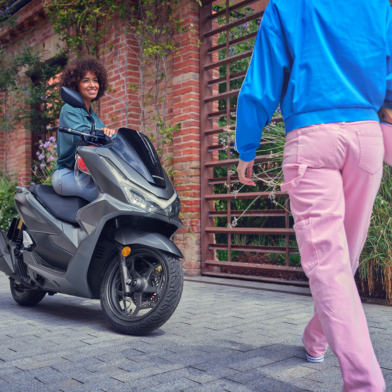 Un modello incontra un amico mentre è appoggiato allo sccoter PCX 125.