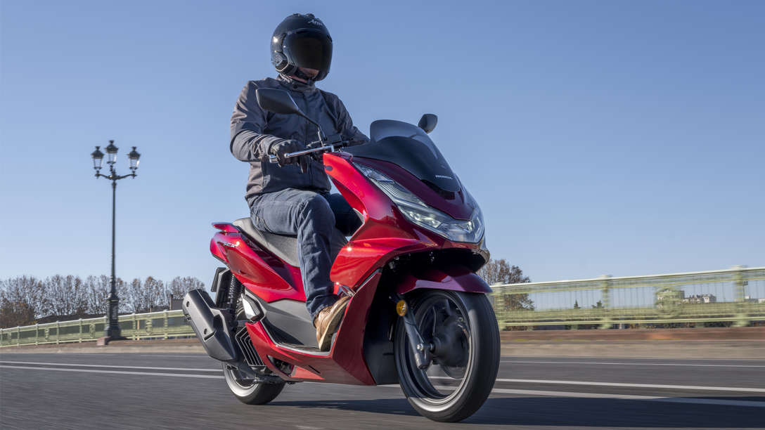 Honda PCX 125 - vista anteriore di tre quarti destra, parcheggiato, guidatore in piedi accanto alla moto grigia