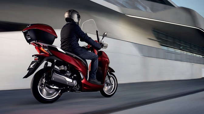 Vista posteriore di tre quarti di uno scooter Honda SH300i con portaoggetti superiore, in città.