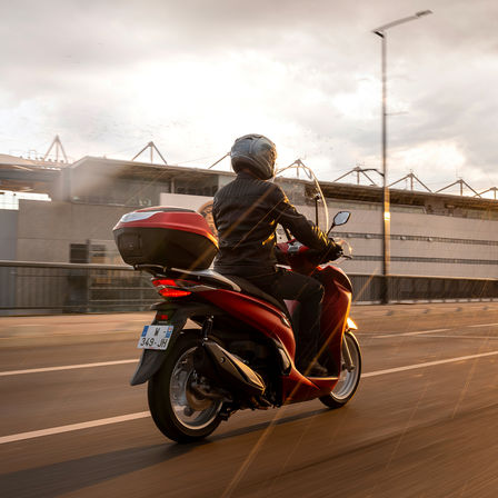 Honda SH350i, vista posteriore di tre quarti destra, con guidatore, moto rossa