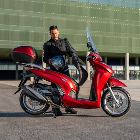 Honda SH350i, uomo in piedi accanto allo scooter, vista posteriore, moto rossa