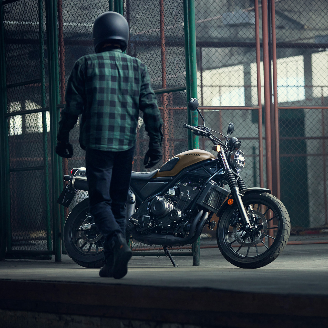 Motociclista che cammina accanto a una Honda CL500 parcheggiata in un magazzino.